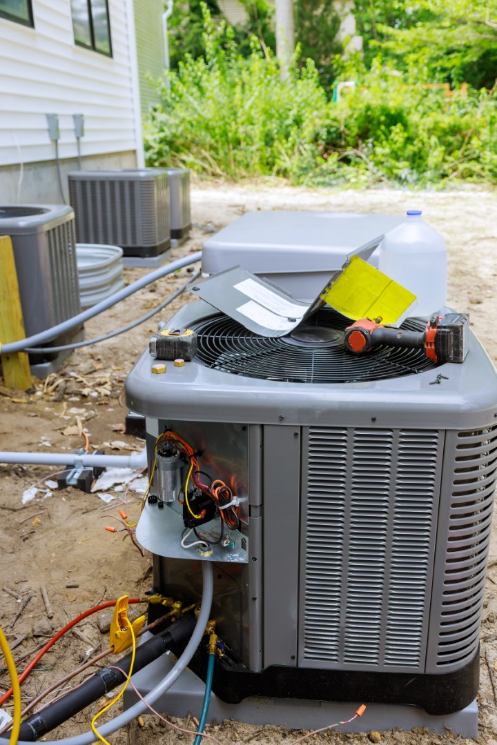 Air conditioning units outside a building, with one unit open for ac repair—wires exposed and tools placed on top during maintenance.